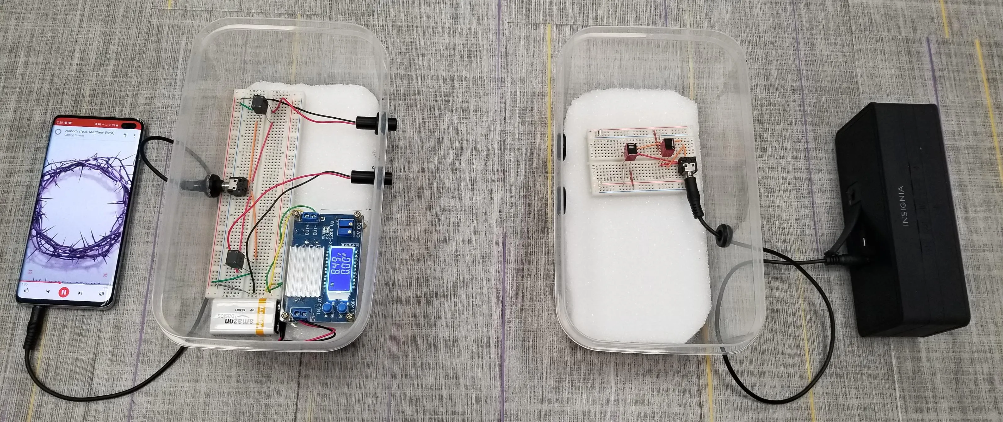 The working stereo setup: a phone playing music feeds a breadboard transmitter in a clear box, which sends two laser beams to a receiver breadboard that drives a powered speaker.